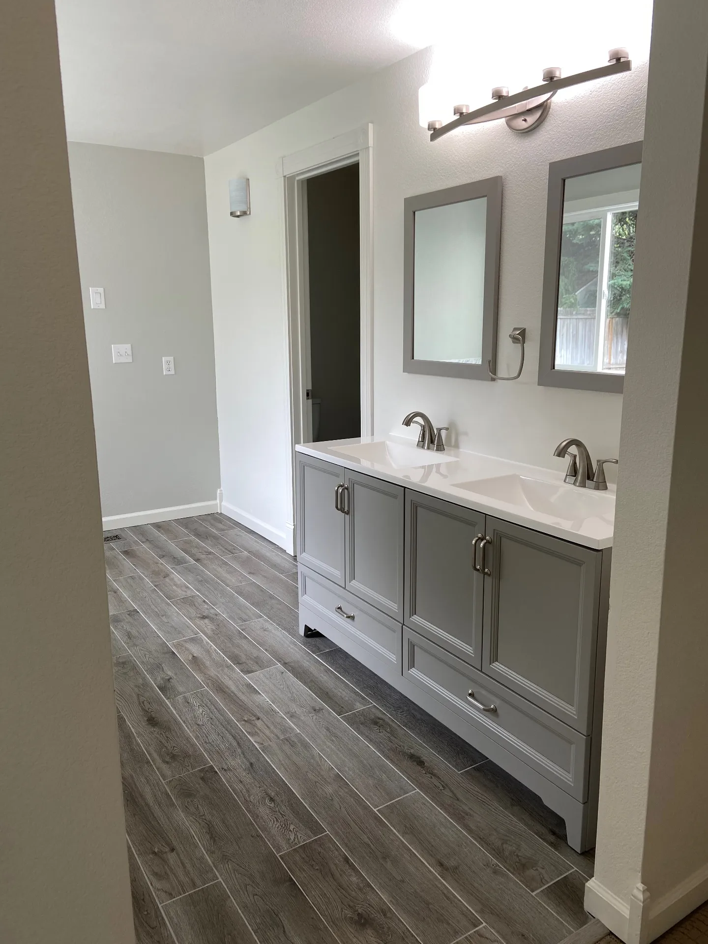 New double vanity with gray cabinets and wood-look tile flooring